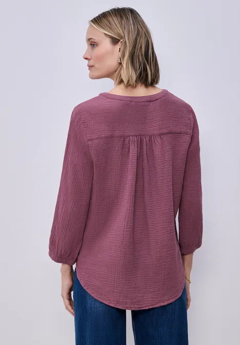 Frau von hinten in weinroter Bluse mit Falten und blauen Jeans, mittellange Haare.